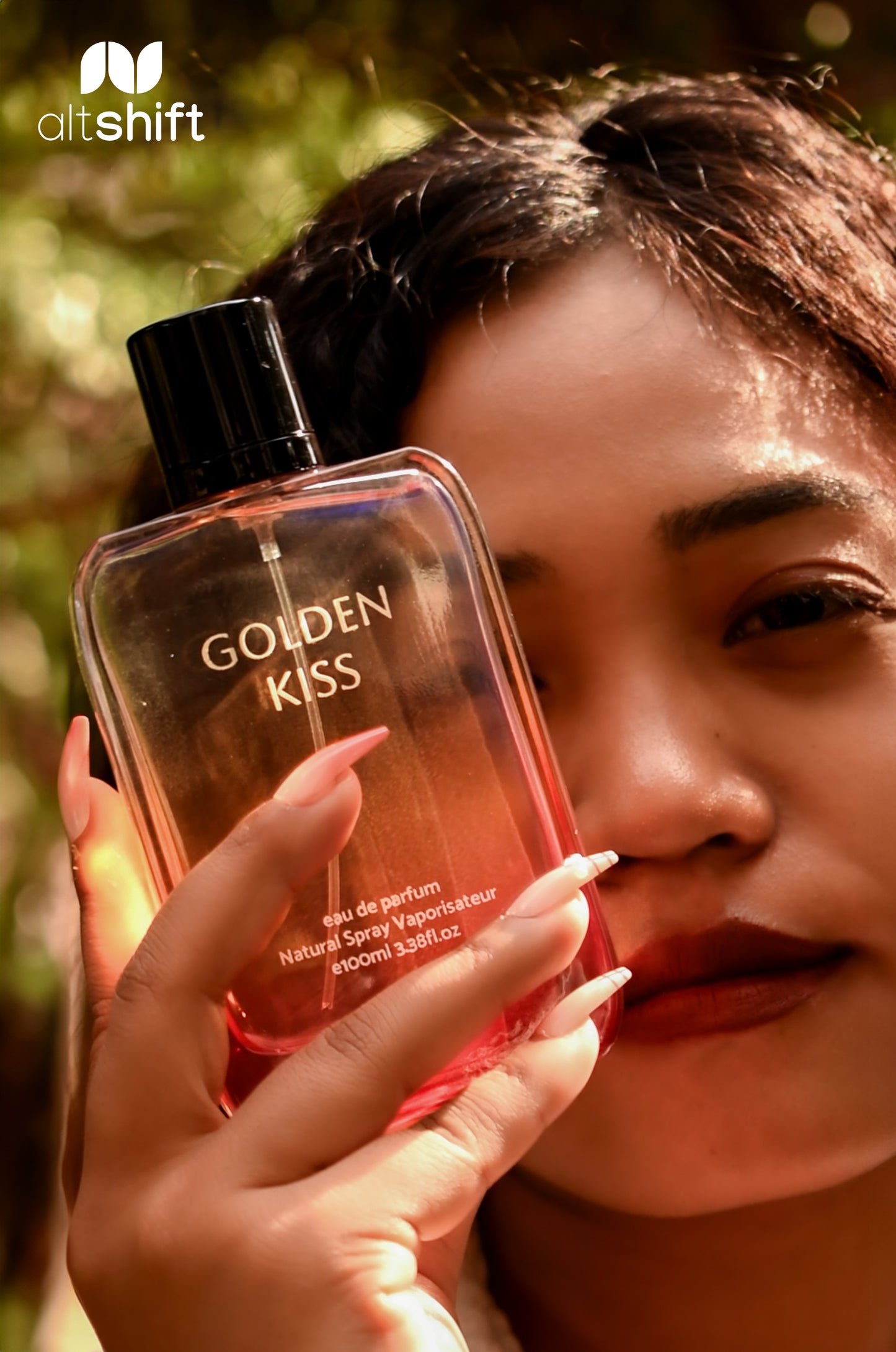 Person holding a perfume bottle labeled 'Golden Kiss' with a blurred natural background